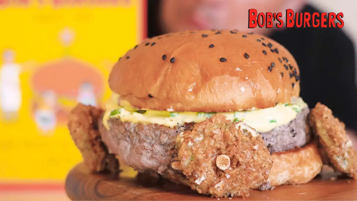 Battered pickle wheels pinned around a thick patty with green-flecked sauce under a sesame bun