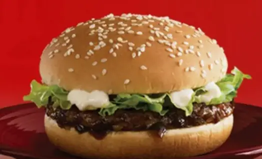 Close-up of a beef patty with shredded lettuce in a sesame seed bun