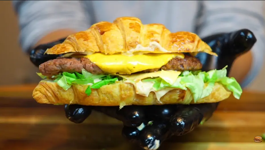 Close-up of a beef patty with melted American cheese and pickles in a croissant