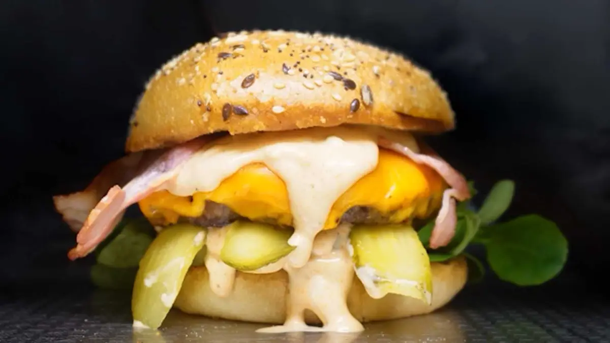 Close-up of a beef patty with mimolette and pickles in a brioche bun