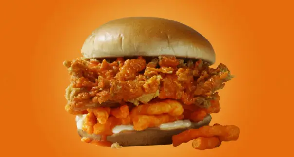 Close-up of a breaded chicken fillet in a brioche bun, hot sauce at the edge