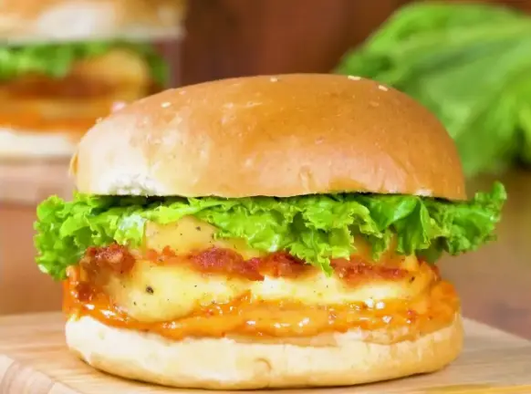 Close-up of a fried paneer slab with shredded lettuce in a soft burger bun