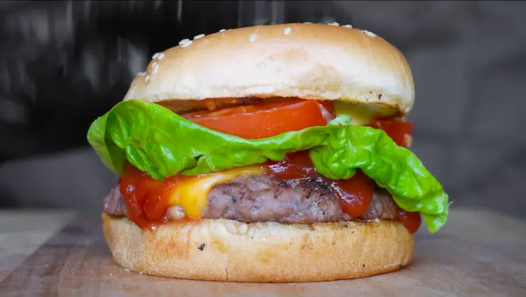 Close-up of a beef patty with melted American cheese in a sesame seed bun