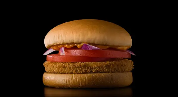 Close-up of a burger patty with red onion rings in a soft burger bun