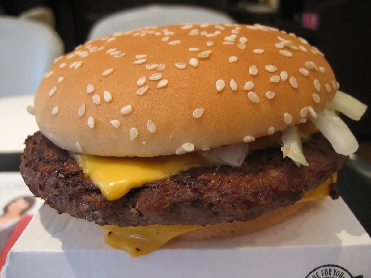 Close-up of a beef patty with melted American cheese in a sesame seed bun
