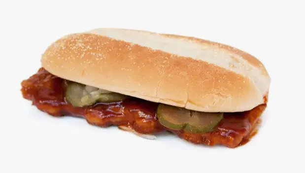 Close-up of a pork patty with diced onion and pickles in a long roll