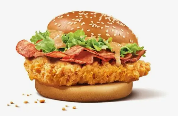 Close-up of a fried chicken thigh with shredded lettuce in a sesame seed bun
