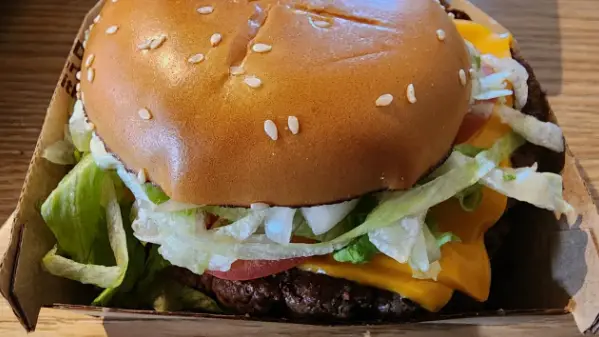 Close-up of a beef patty with melted American cheese in a sesame seed bun