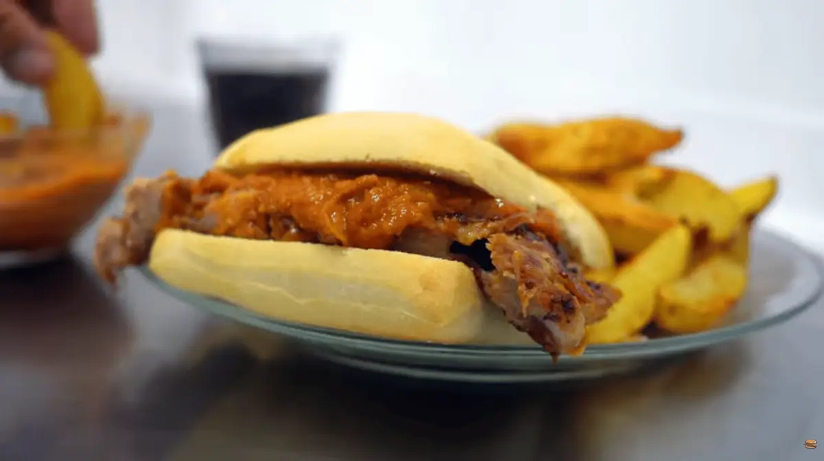 Close-up of slow-cooked pork rib meat with diced onion and peppers in a long roll