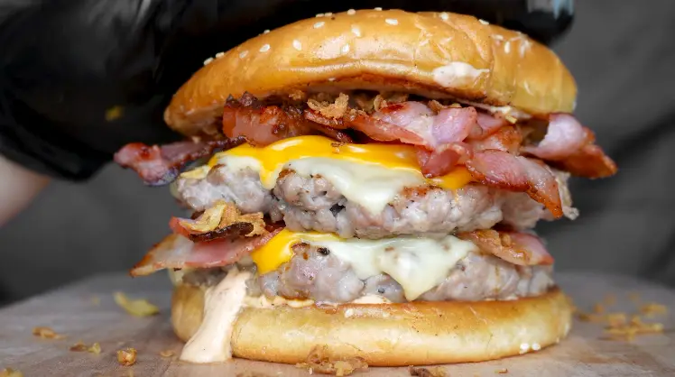 Close-up of a pork patty with gouda and bacon in a sesame seed bun