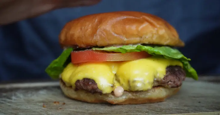 Close-up of a beef patty with melted American cheese and pickles in a brioche bun