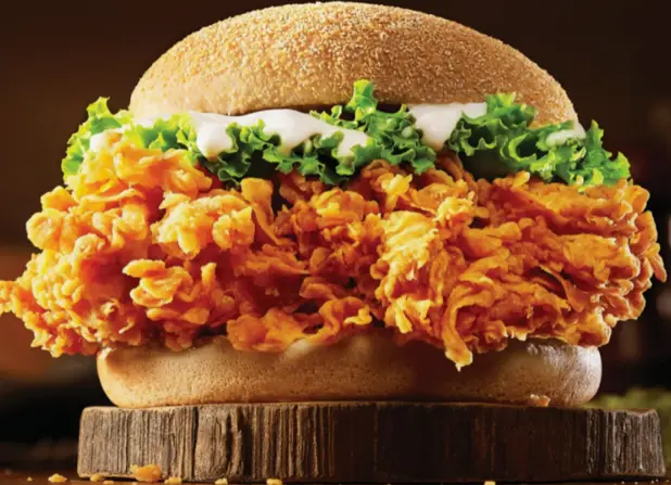 Close-up of a breaded chicken fillet with shredded lettuce in a soft burger bun