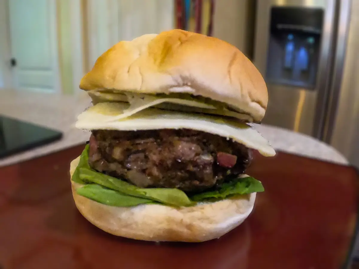 Close-up of a beef patty with red onion rings served open, mustard at the edge