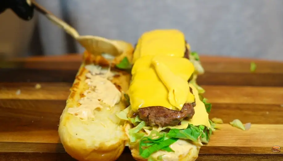 Close-up of a beef patty with melted American cheese and pickles in a baguette