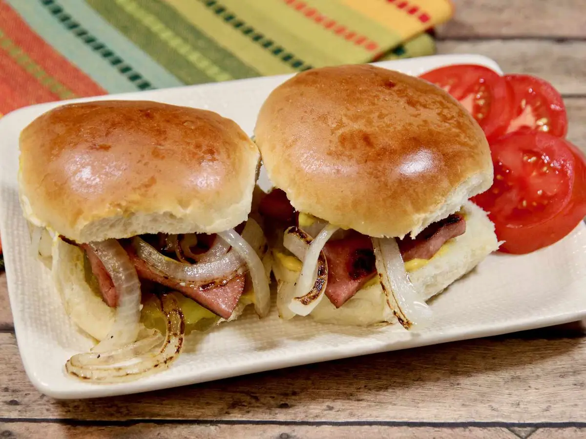 Close-up of fried bologna with pickles and diced onion in a slider roll