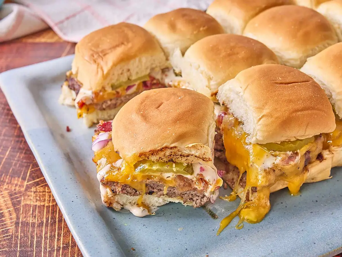 Close-up of a beef patty with melted cheddar and bacon in a slider roll