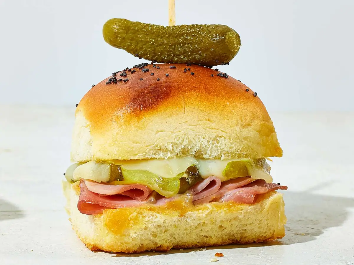 Close-up of a burger patty with Swiss cheese, ham and pickles in a slider roll
