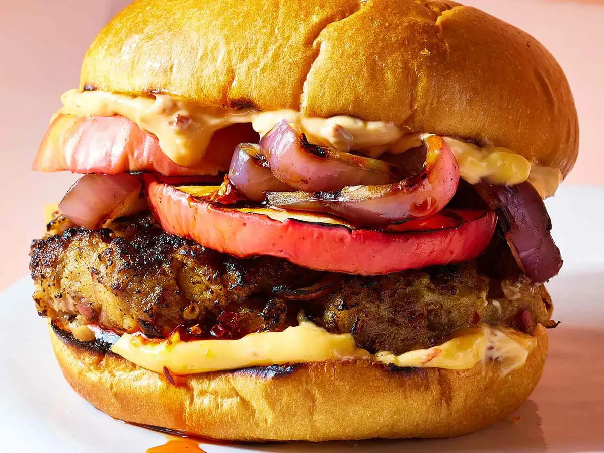 Close-up of a beef patty with red onion rings in a soft burger bun