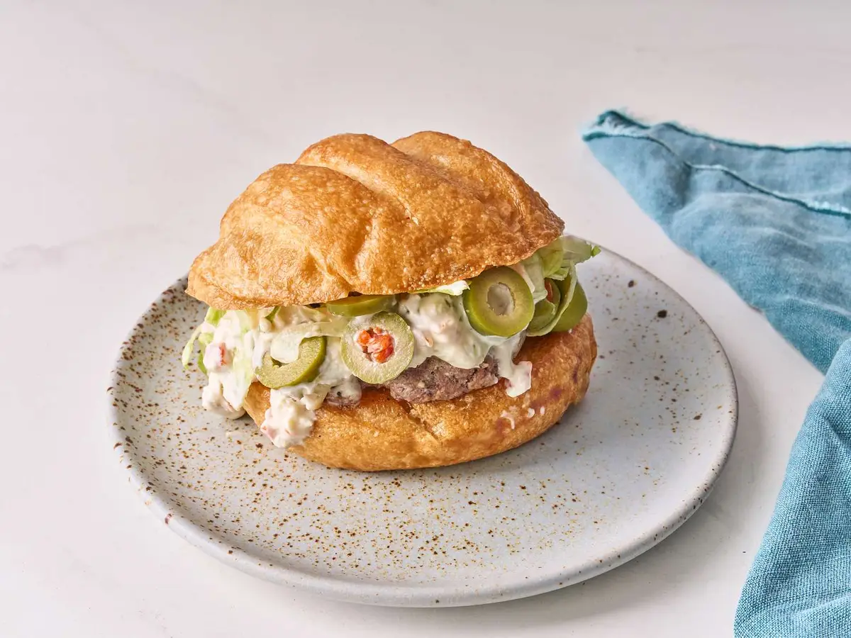 Close-up of a beef patty with Swiss cheese and olives in a soft burger bun