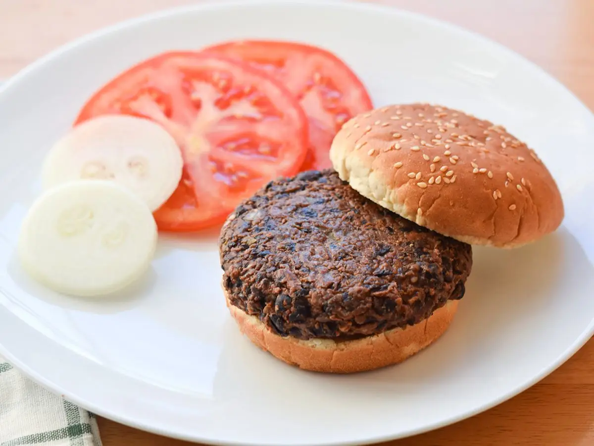 Close-up of a black bean patty with diced onion and peppers in toasted bread
